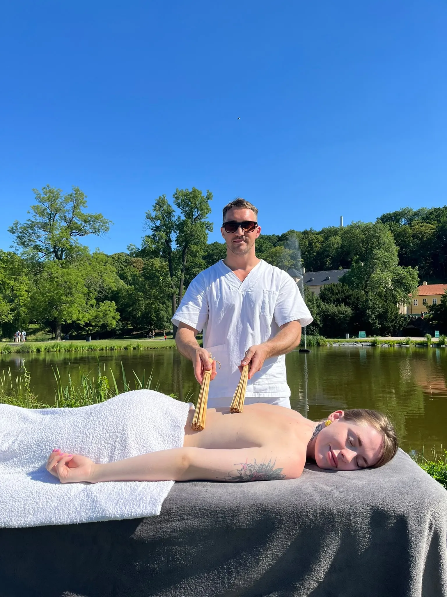 A bamboo stick massage on a client's back, outdoors by a lake
