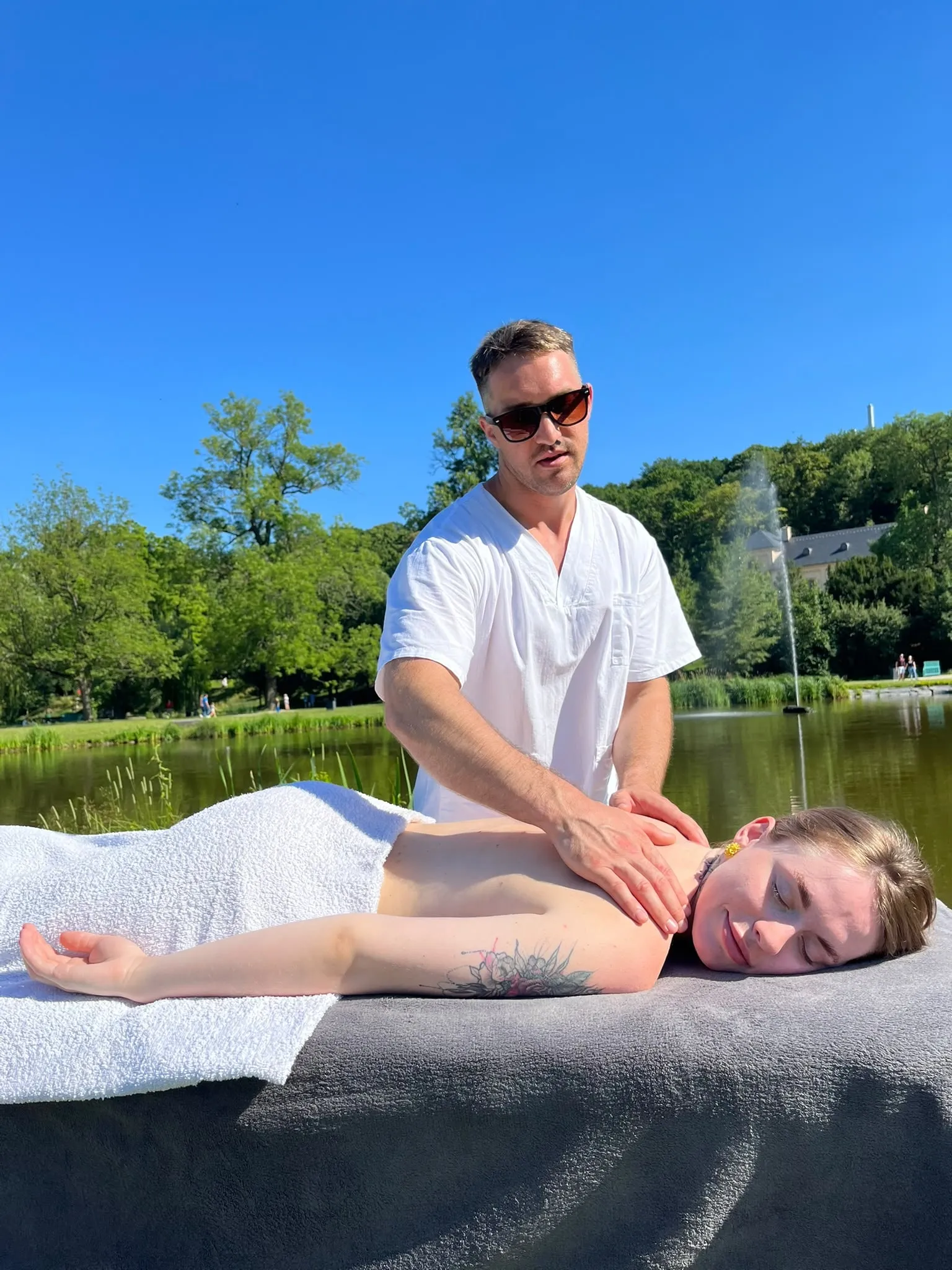 A shoulder massage outdoors by a lake, the client relaxed on a portable table with white towels